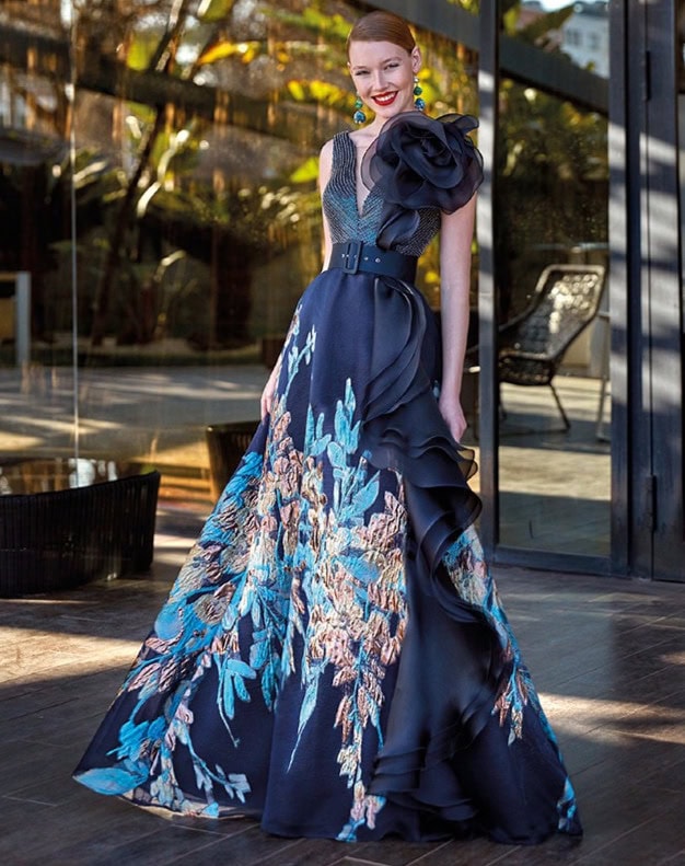 Robe de soirée longue en tissu fluide avec motif floral bleu et or, ornée d’un grand détail en tissu noir sur l’épaule, idéale pour événements formels ou galas.