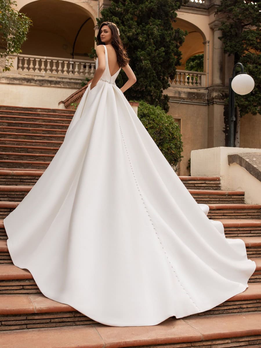 Robe de mariée élégante avec traîne longue et détails sophistiqués, portée par une modèle sur un escalier historique en plein air, ambiance chic et romantique.