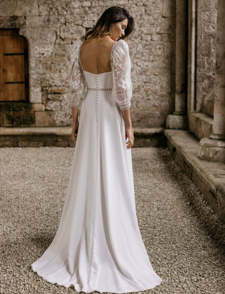 Robe de mariée élégante avec manches en dentelle et dos nu, parfaite pour une cérémonie romantique dans un cadre historique.