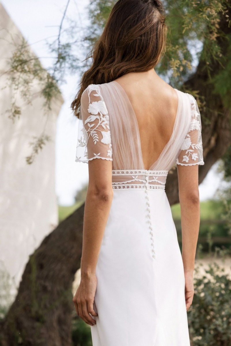 Élégante robe de mariée blanche avec détails en dentelle et dos nu, portée par une femme dans un cadre naturel en plein air, idéale pour un mariage romantique en extérieur.
