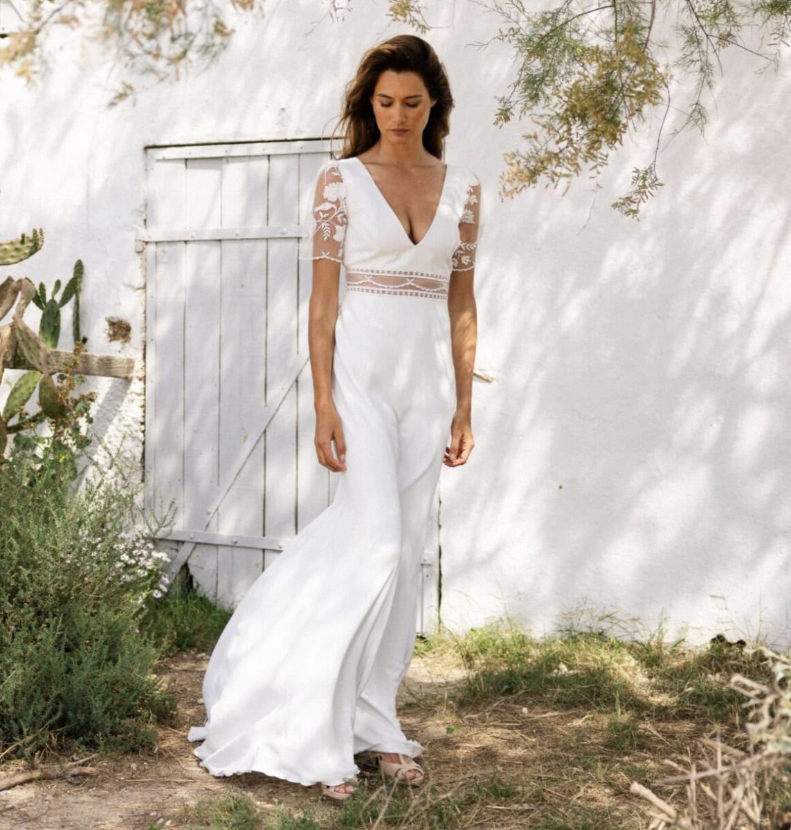 Vêtement de mariage blanc élégant avec dentelle, manches courtes et décolleté en V, porté par une femme dans un jardin ensoleillé, ambiance bohème chic.