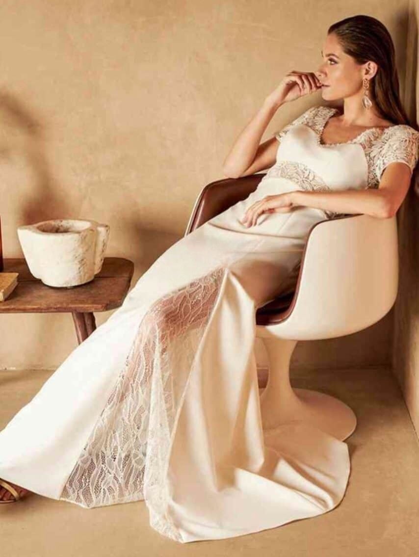 Une femme élégante en robe de mariée blanche assise dans un fauteuil moderne, dans un décor minimaliste avec un pot en céramique à côté.