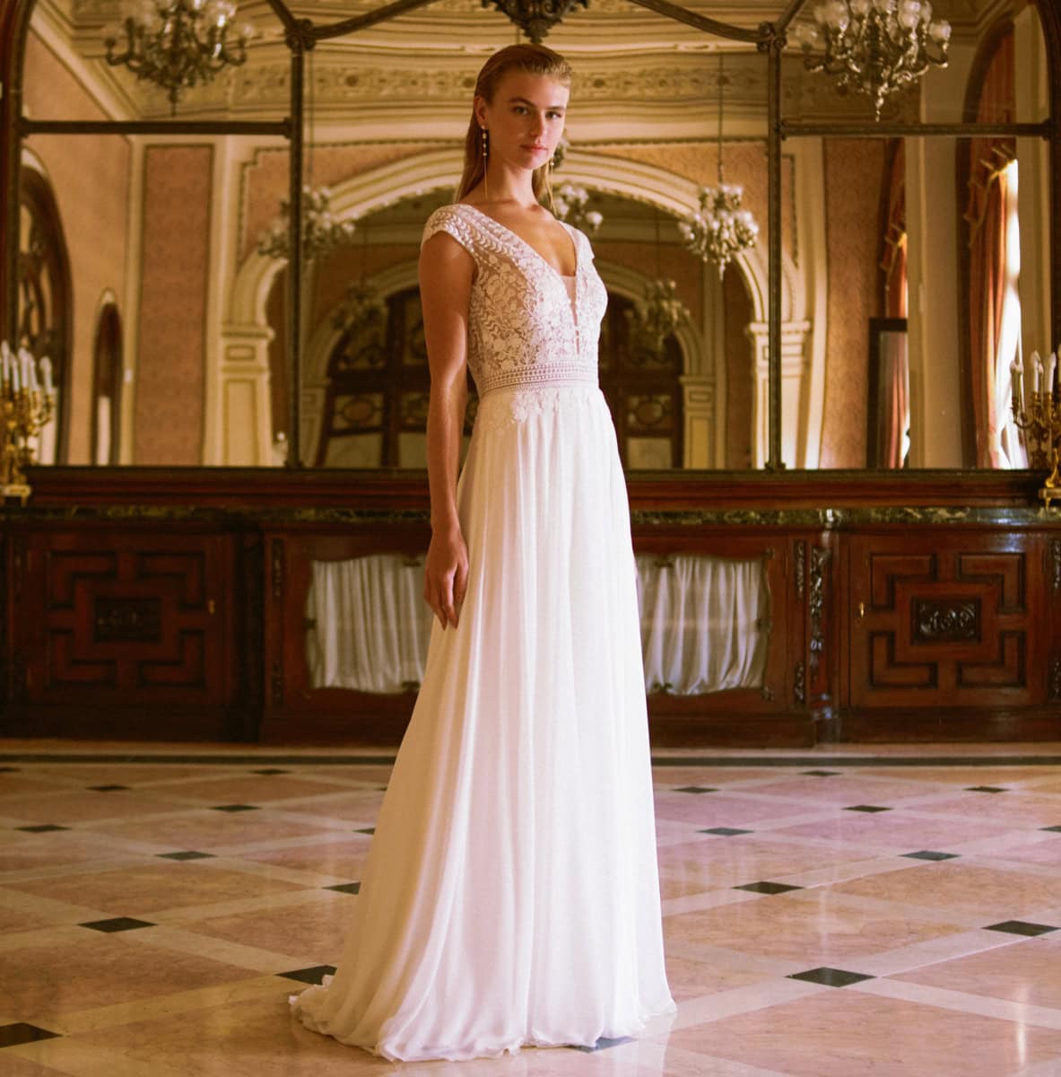 Une femme portant une robe de mariée élégante dans un intérieur somptueux avec architecture classique et lustres en cristal.