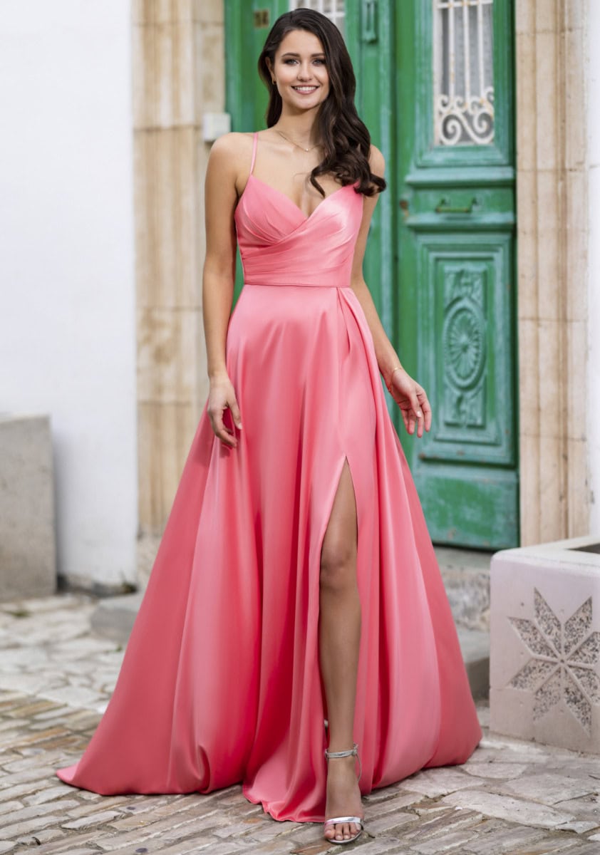 Robe de soirée rose longue avec décolleté en V et fente, portée par une femme souriante devant une porte verte. Parfaite pour une occasion spéciale ou un événement formel.