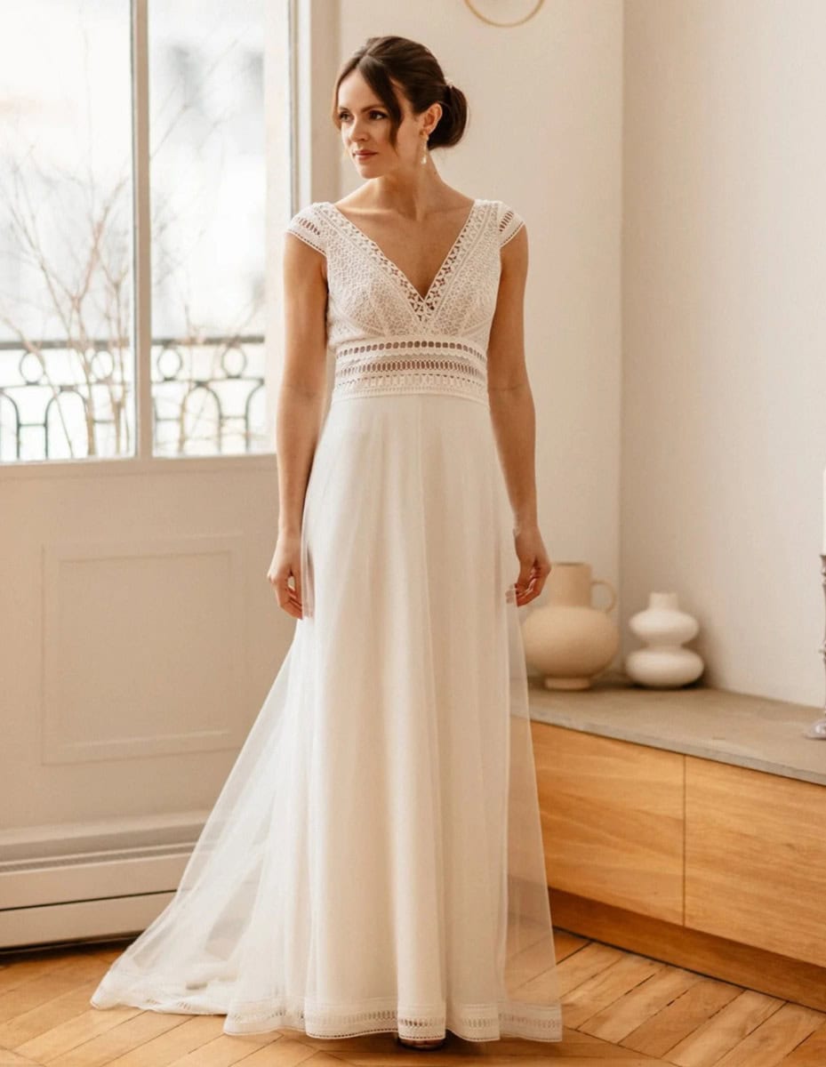 Léger et élégant, robe de mariée en dentelle ivoire avec décolleté en V, manches courtes et jupe fluide, parfaite pour une cérémonie nuptiale romantique dans un intérieur lumineux.