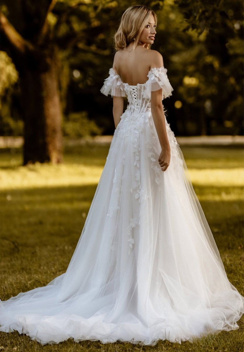Robe de mariée blanche élégante avec détails en dentelle et manches courtes en tulle, portée par une femme dans un parc en plein air, ambiance romantique et sophistiquée.