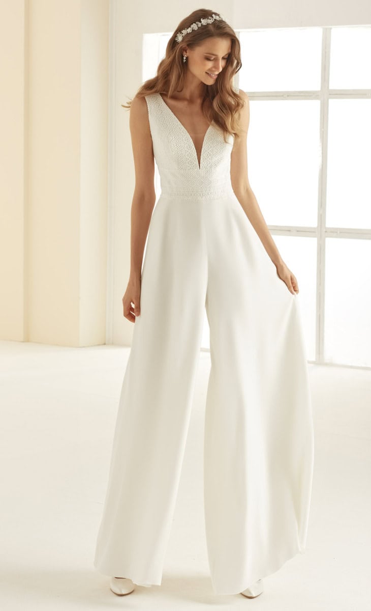 Vêtement de mariée blanc élégant avec décolleté en V profond, détails en dentelle sur le haut, et pantalon fluide pour un look moderne et sophistiqué, parfait pour une mariée chic.