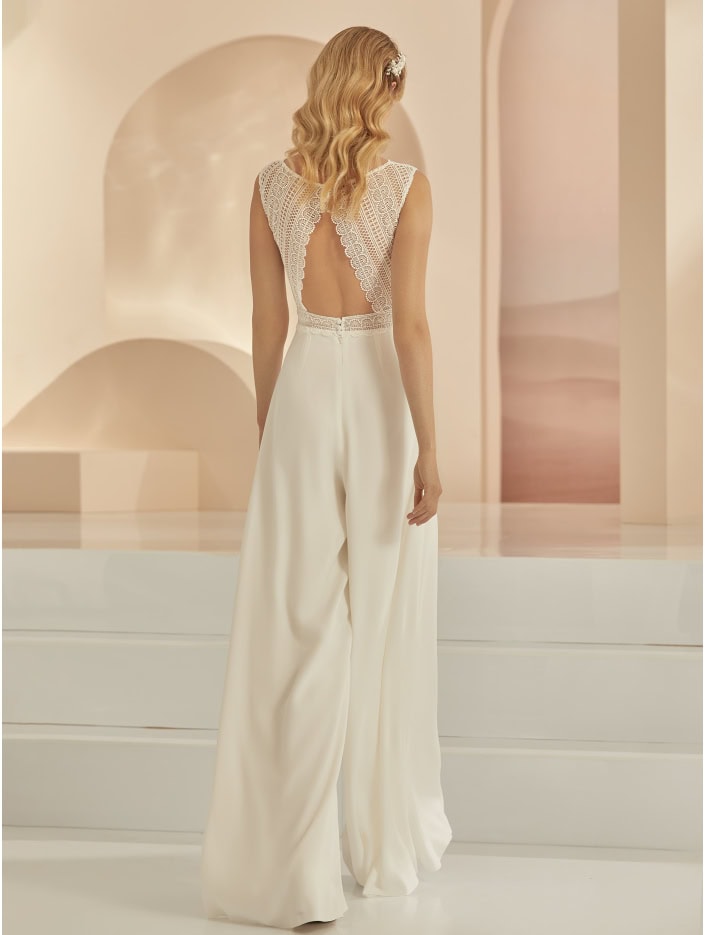 Un robe de mariée élégante avec dos en dentelle et pantalon fluide, parfaite pour une mariée moderne et sophistiquée, dans un décor minimaliste et lumineux.