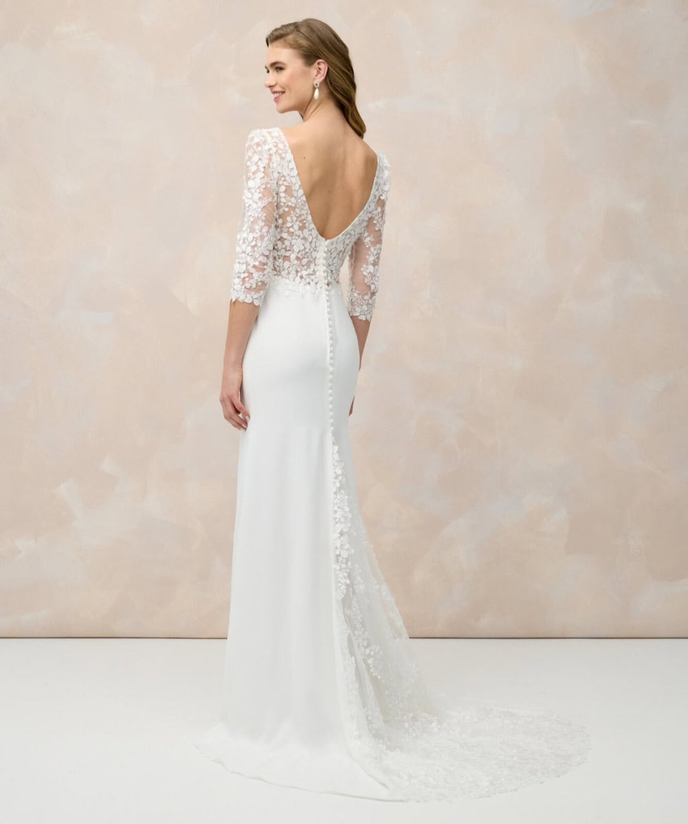 Robe de mariée en dentelle blanche avec manches trois-quarts, dos en V profond et longue traîne, parfaite pour un mariage romantique et sophistiqué.