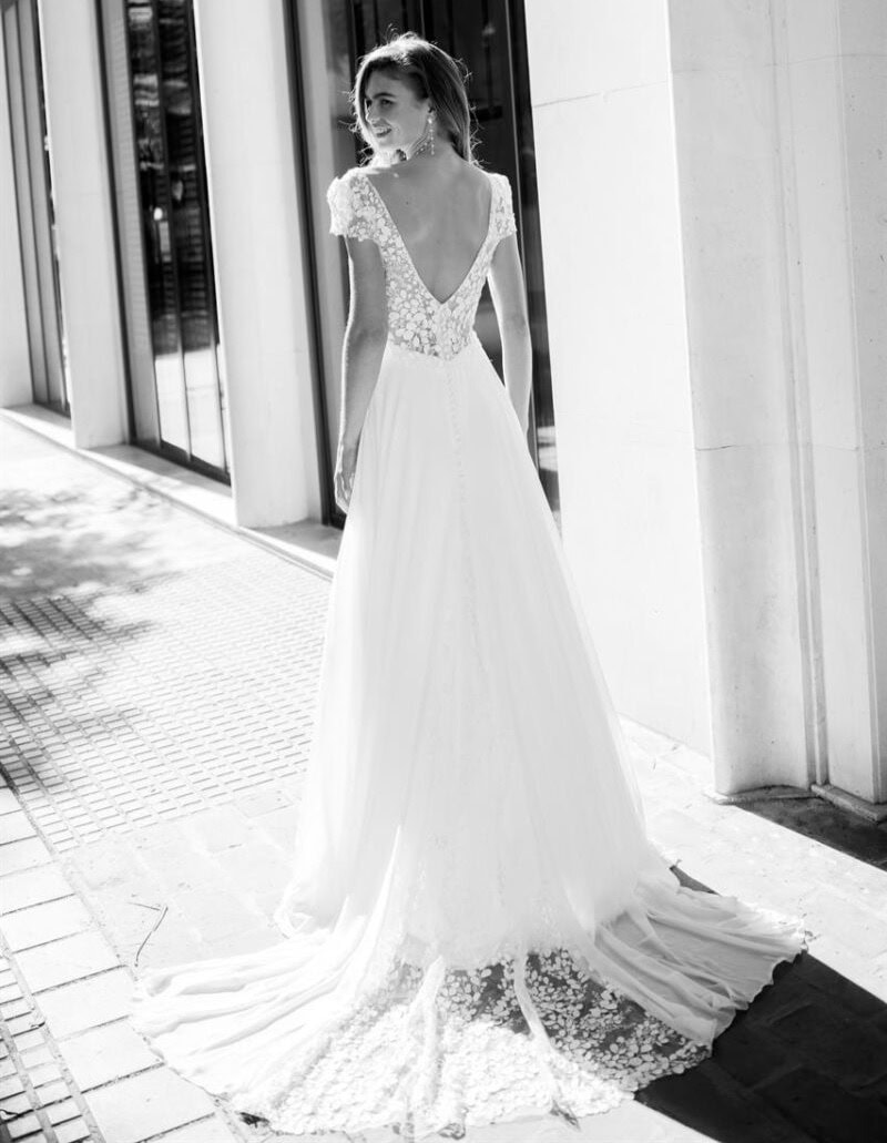 Robe de mariée élégante avec dentelle et dos en V, portée par une femme dans une rue urbaine, en noir et blanc, mettant en valeur le design sophistiqué et romantique.