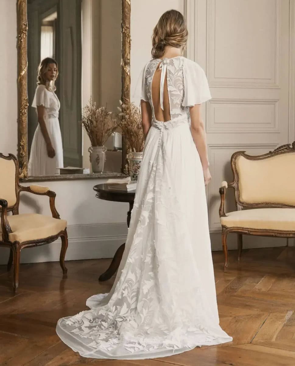 Robe de mariée en dentelle blanche avec dos ouvert et manches courtes, élégante et sophistiquée, parfaite pour un mariage romantique dans un intérieur classique.
