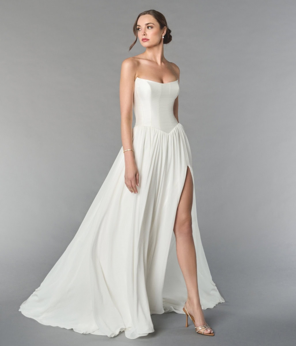Robe de mariée blanche élégante avec décolleté bustier et fente haute, parfaite pour mariage ou occasion spéciale, sur fond gris neutre.