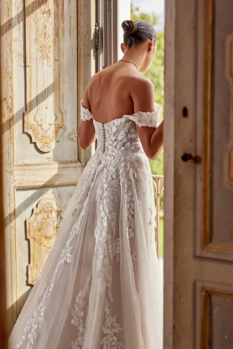 Robe de mariée en dentelle blanche avec bustier corseté et manches courtes, vue de dos, dans un décor vintage avec lumière naturelle.