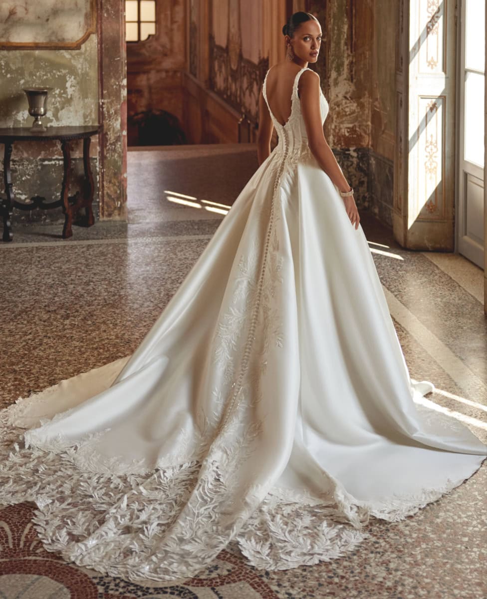 Robe de mariée blanche avec traîne longue, détails en dentelle et dos nu, dans un décor vintage lumineux. Parfaite pour une mariée sophistiquée et romantique.