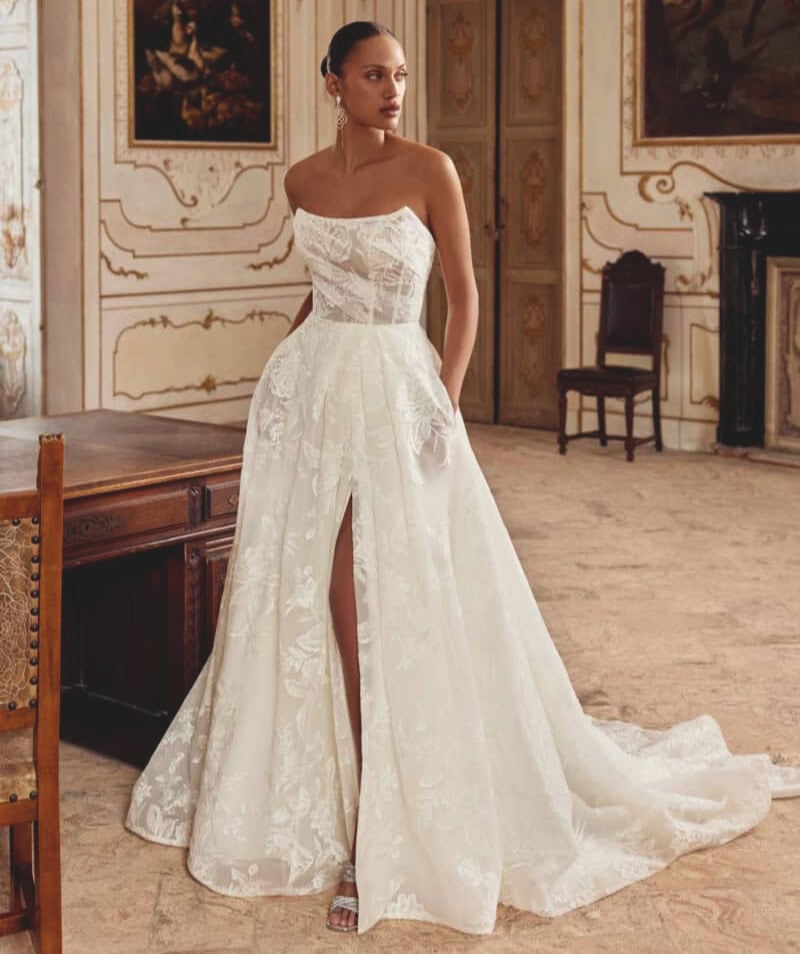 Robe de mariée en dentelle blanche avec décolleté asymétrique et jupe fluide, parfaite pour un mariage élégant. Conçue pour mettre en valeur la silhouette, cette robe allie sophistication et modernité.