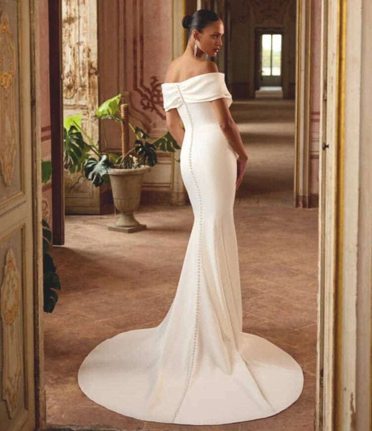Robe de mariée sophistiquée avec décolleté épaule et traîne élégante.