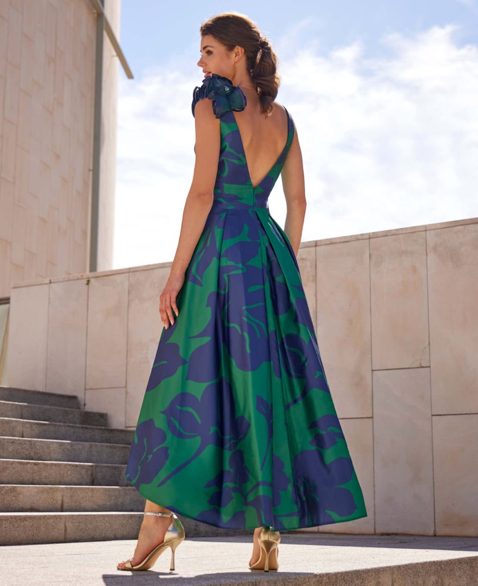 Robe longue à motifs verts et bleus avec épaules à volants, idéale pour une occasion spéciale, portée par une femme sur un escalier en extérieur.