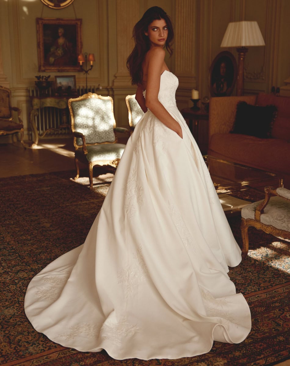 Vêtement de mariée blanc avec une robe de bal longue et détails délicats, portée par une femme dans un intérieur sophistiqué.