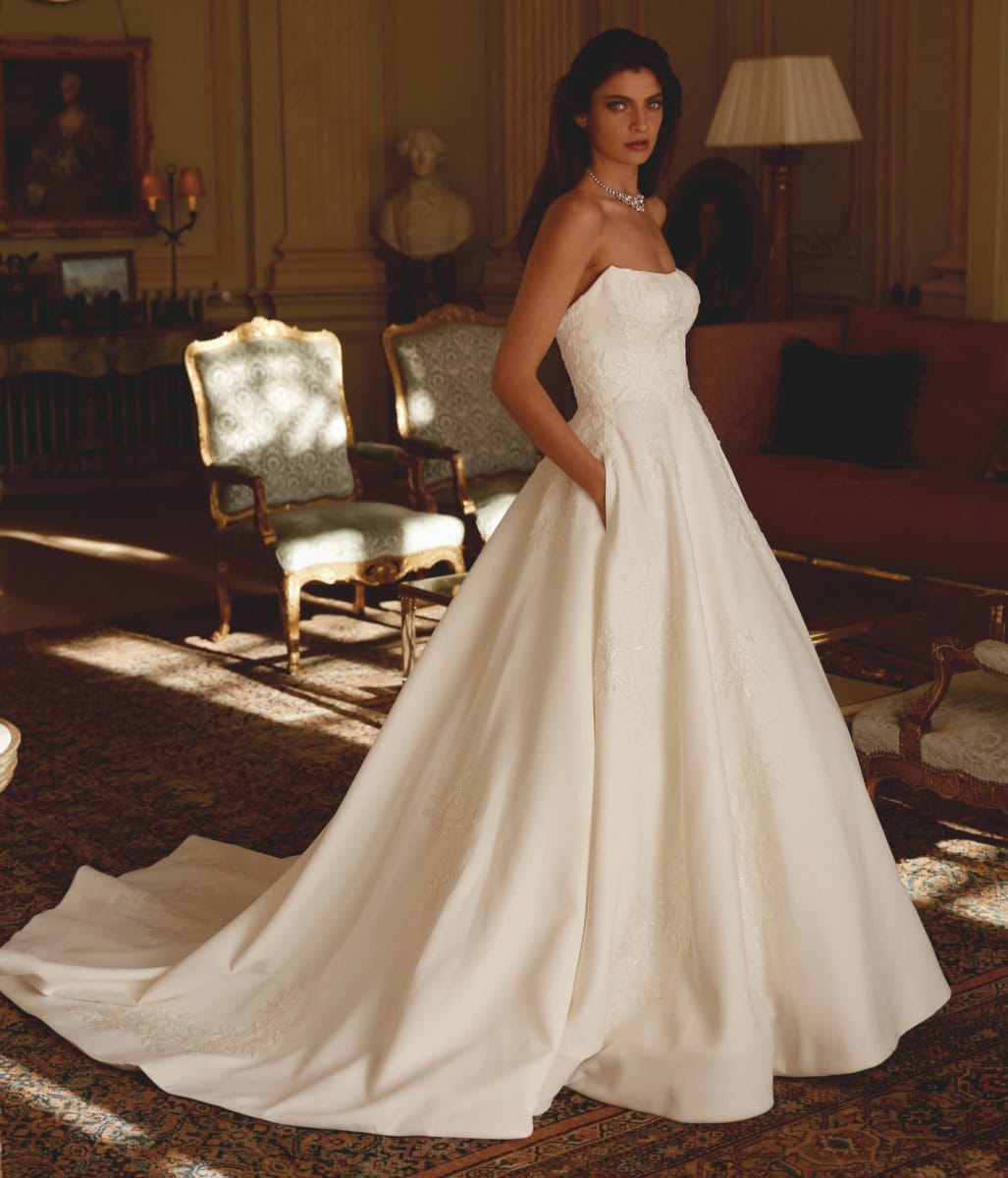 Robe de mariée blanche élégante avec bustier en dentelle et jupe volumineuse, portée par une femme dans un salon sophistiqué avec mobilier ancien et éclairage tamisé.