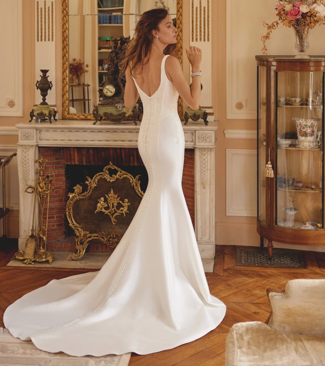 Robe de mariée blanche longue, élégante et raffinée, portée par une femme dans un intérieur vintage, mettant en valeur un style classique et chic pour un mariage.
