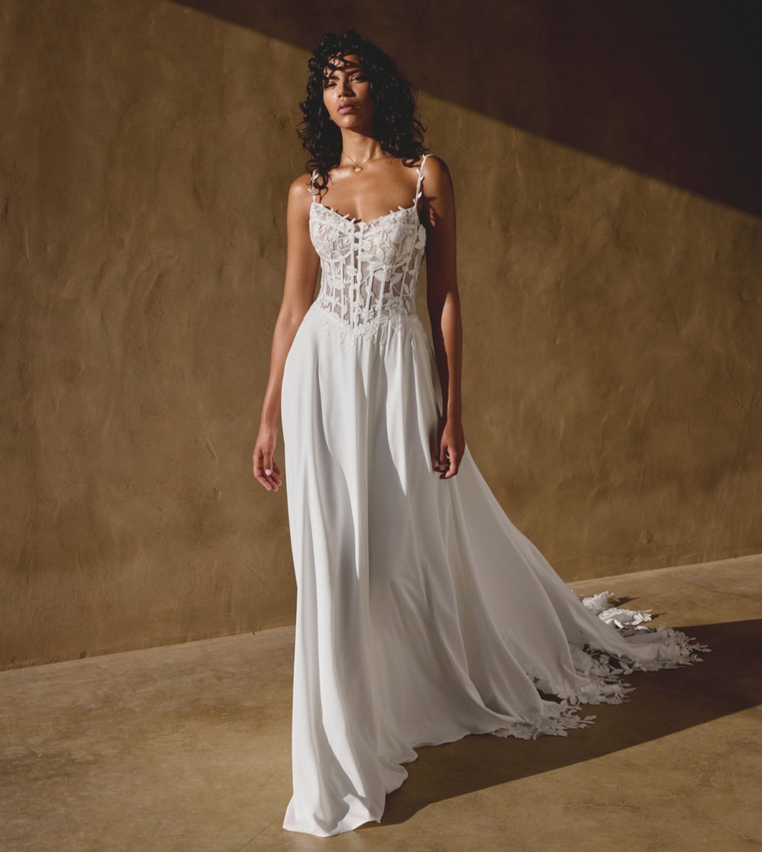 Légère robe de mariée blanche en dentelle avec bretelles fines, style bohème chic, portée par une femme aux cheveux bouclés, dans un décor minimaliste avec lumière naturelle.