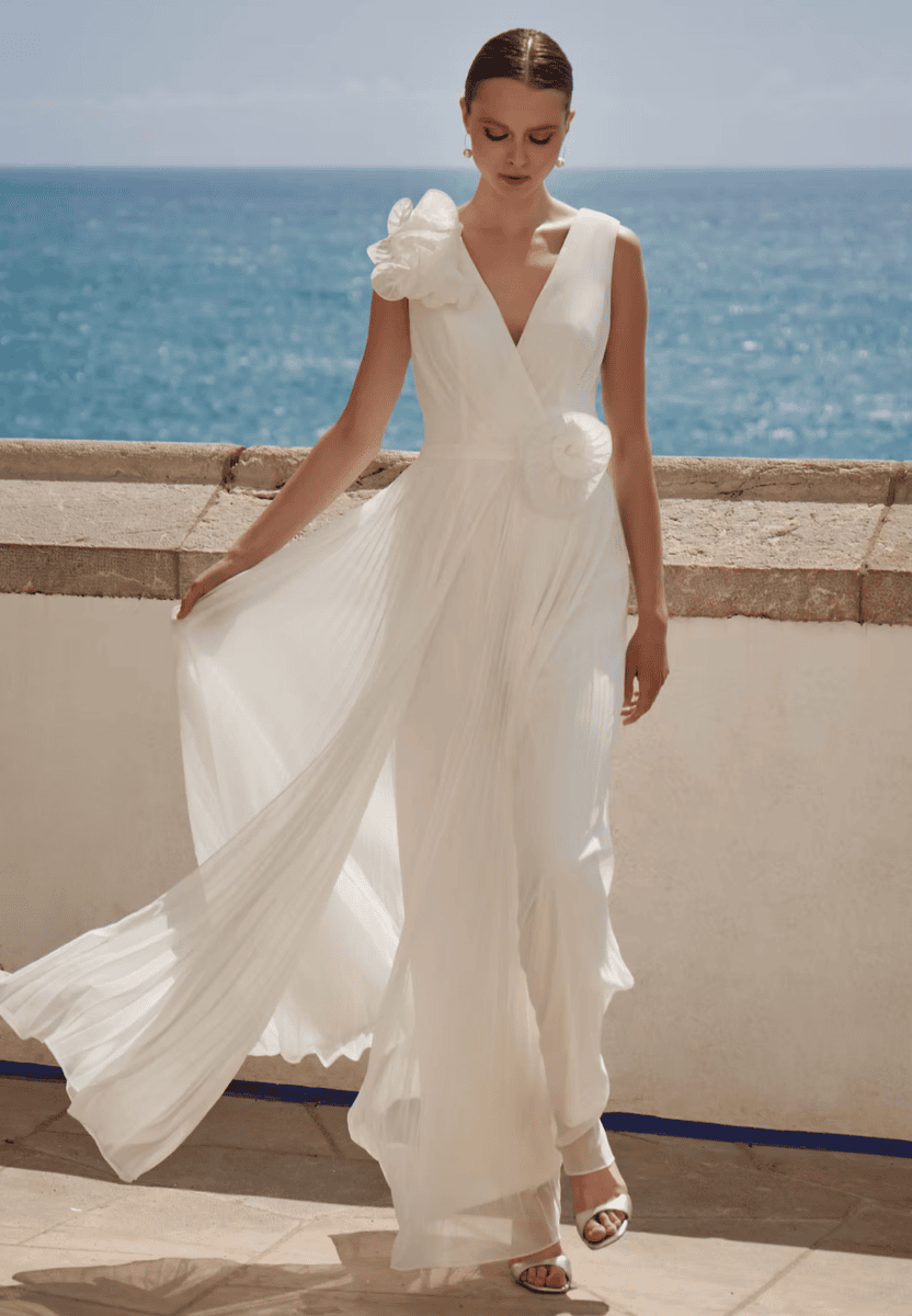 Robe de mariée blanche élégante avec détails floraux sur l'épaule, vue sur la mer en arrière-plan.
