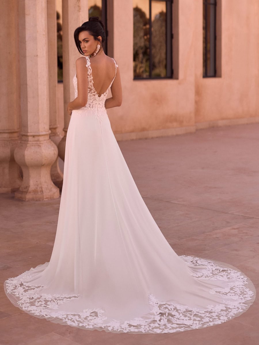 Une robe de mariée élégante avec dentelle et dos nu, portée par une femme dans un lieu architectural en pierre, ambiance romantique et sophistiquée.