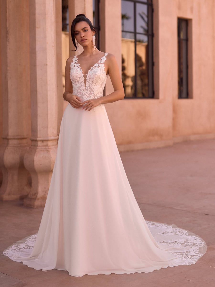 Vêtement de mariage élégant avec dentelle florale sur le haut et jupe fluide en tissu léger, porté par une femme devant un bâtiment en pierre dans un style architectural classique.