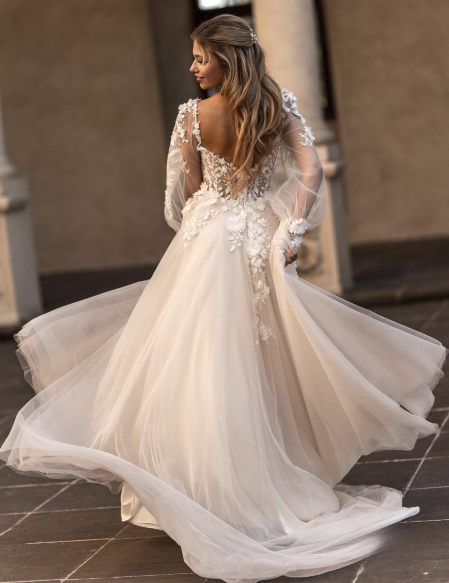 Un magnifique robe de mariée en tulle ivoire avec détails en dentelle florale, manches longues transparentes et dos en V, idéale pour un mariage élégant et romantique.