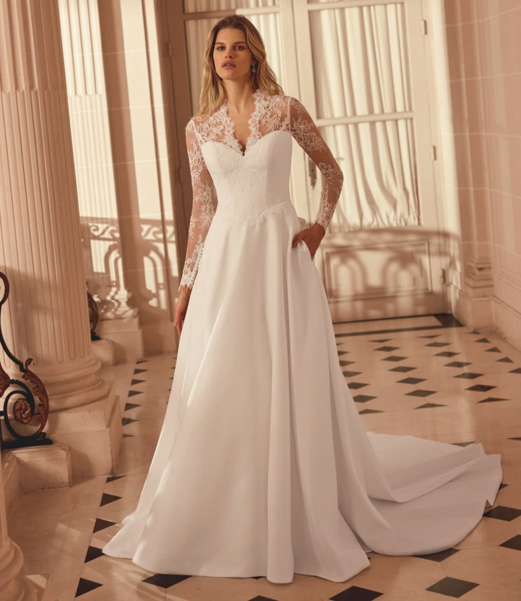 Robe de mariée élégante avec dentelle et décolleté en V, portée par un mannequin dans un décor classique et lumineux.