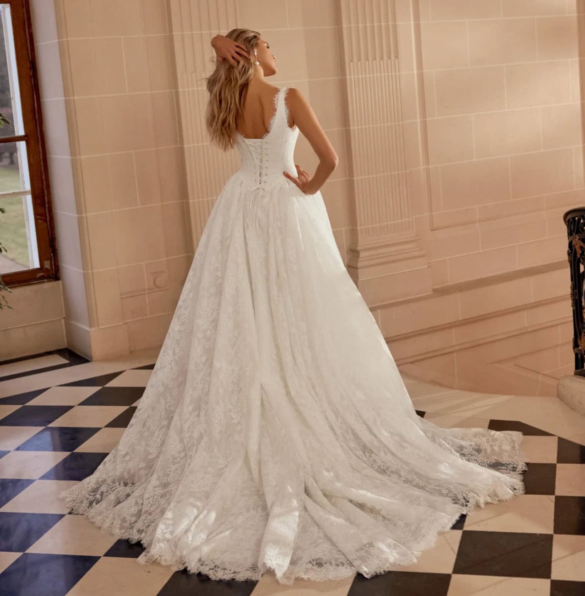Robe de mariée élégante en dentelle blanche avec traîne longue, portée par une femme dans un intérieur sophistiqué.