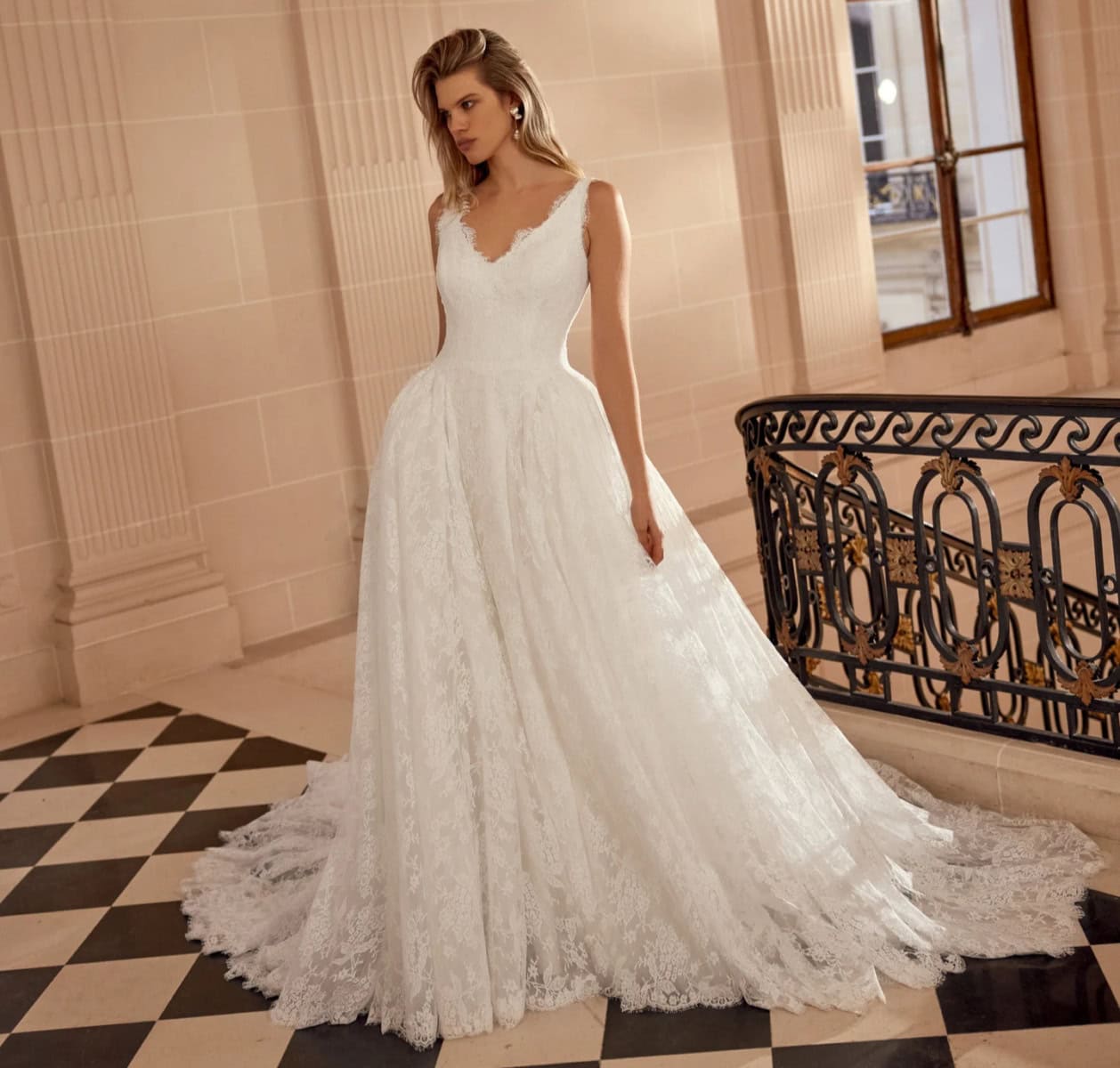 Robe de mariée blanche en dentelle avec décolleté en V et taille cintrée, portée par une femme dans un intérieur élégant.