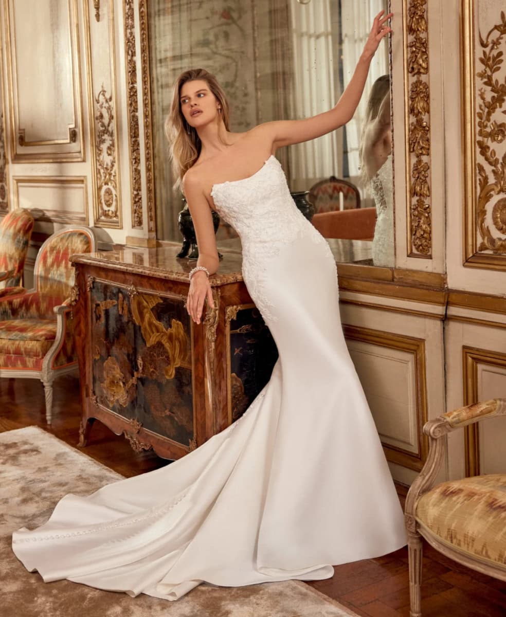 Femme en robe de mariée blanche élégante dans un décor luxueux avec miroirs dorés et meubles anciens.