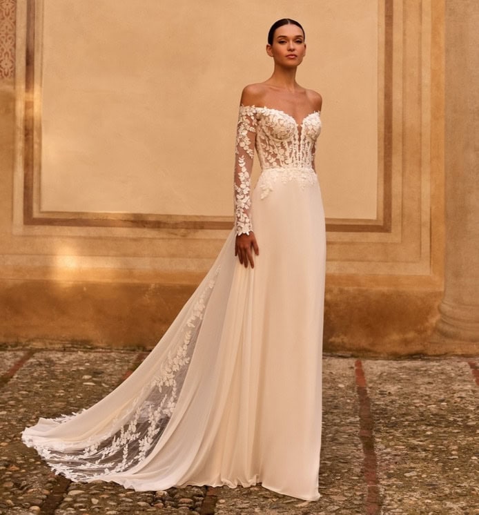 Vêtement de mariée élégant avec corsage en dentelle et longue traîne en tissu fluide, porté par un mannequin dans un décor classique et sophistiqué.
