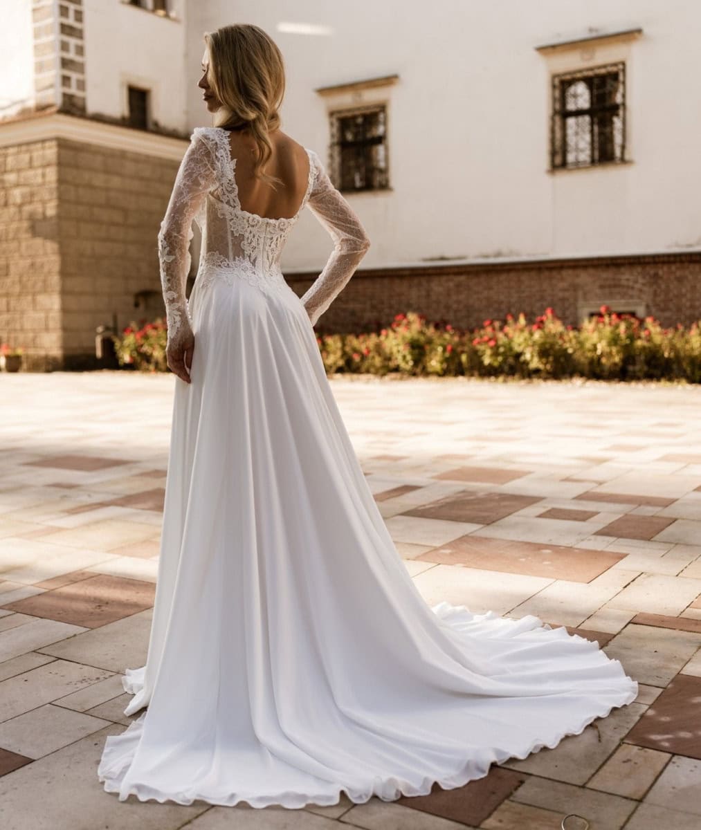 Un magnifique robe de mariée blanche avec dentelle, longue traîne, portée par une femme dans un cadre historique en plein air, mettant en valeur l'élégance et la sophistication pour un mariage.