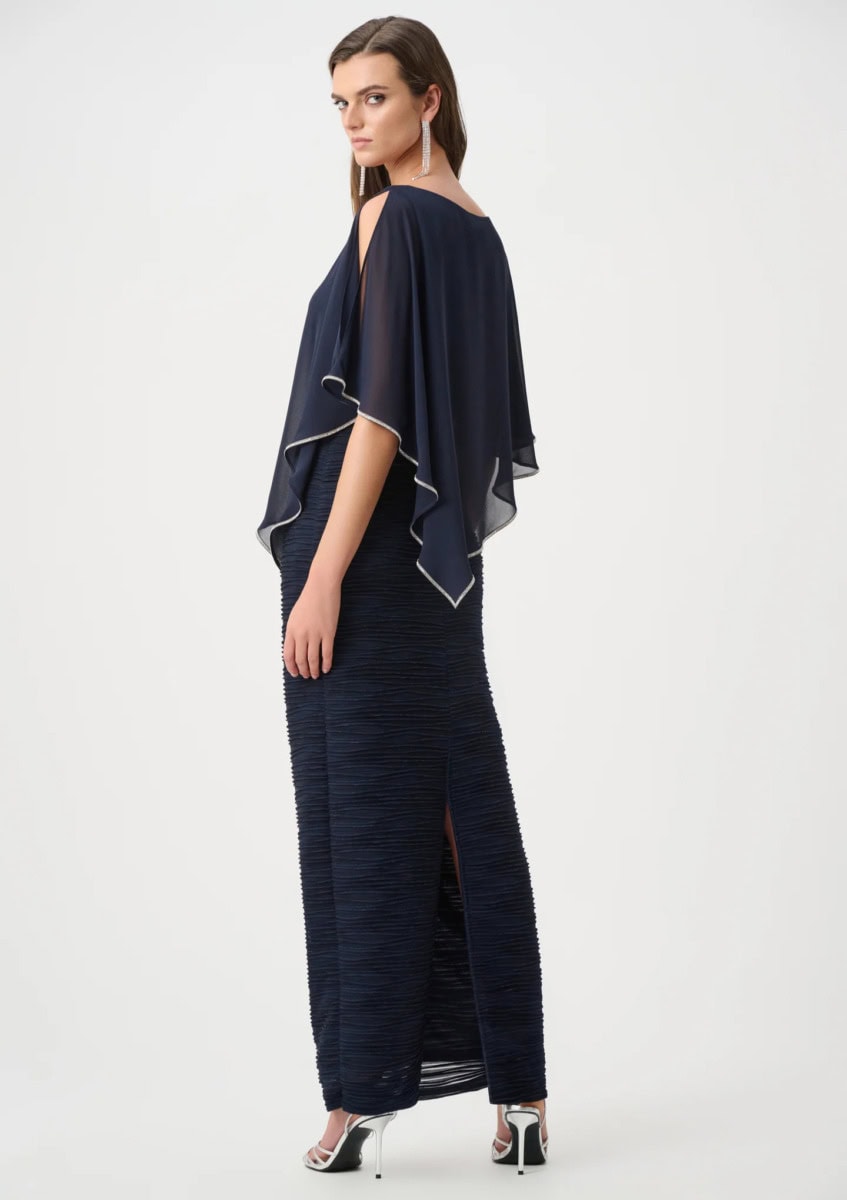 Robe longue élégante en tissu bleu foncé avec cape fluide et détails contrastés, portée par une femme lors d'une séance photo.