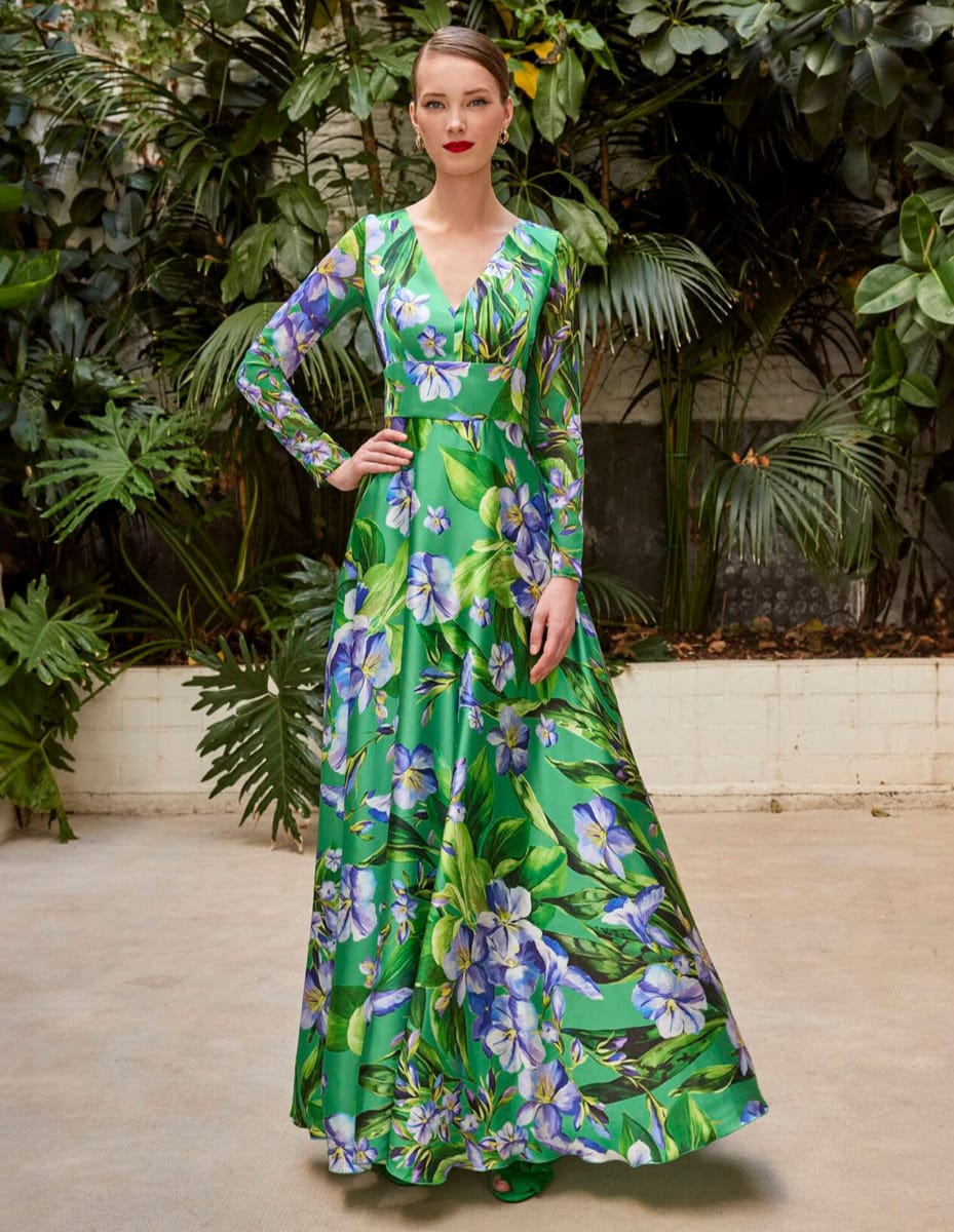 Robe longue florale verte et bleue avec décolleté en V, portée par une femme dans un jardin luxuriant.