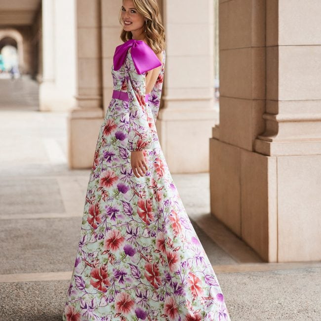 Femme portant une robe longue à fleurs avec détails violets et un col en satin violet, dans un environnement architectural élégant.