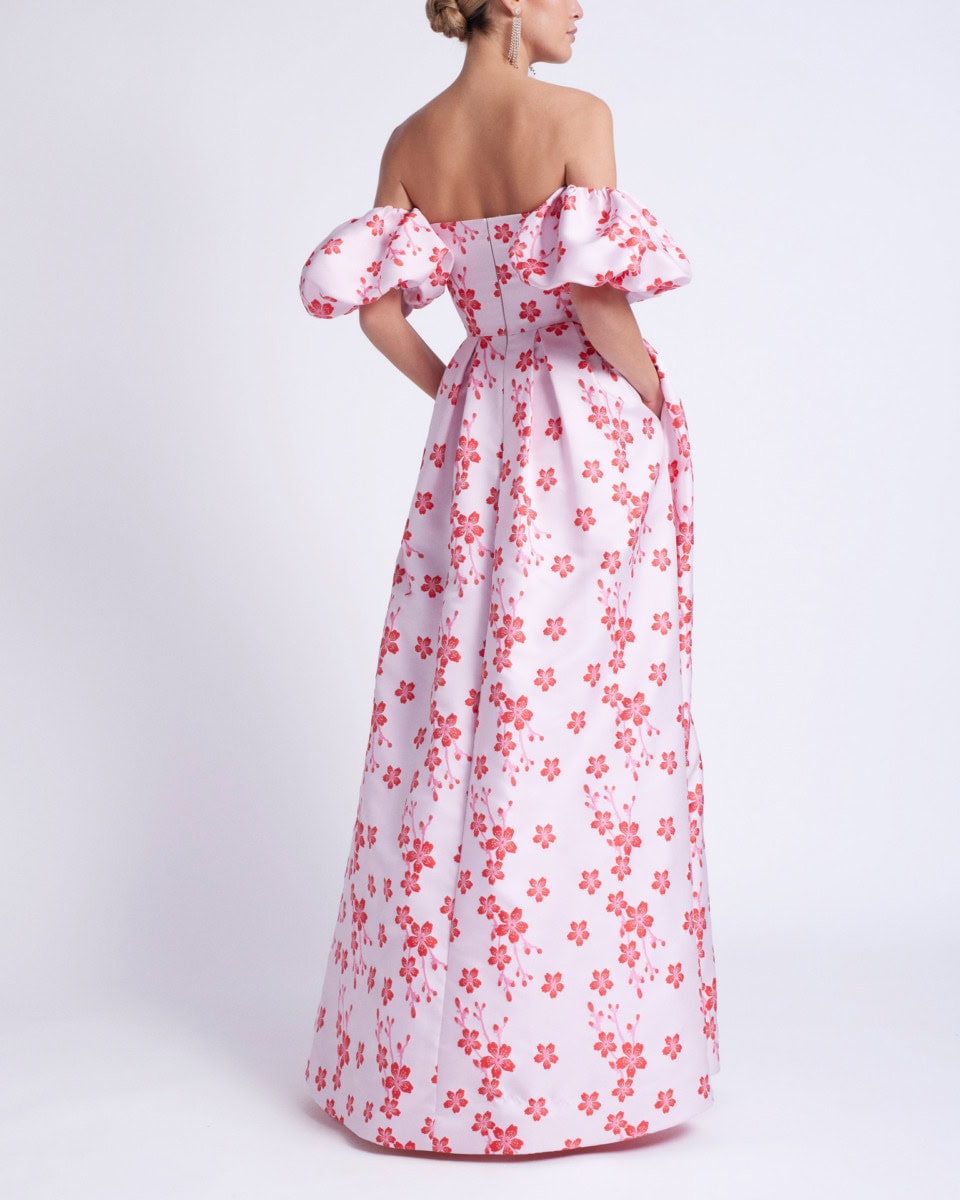 Robe longue blanche à motifs floraux roses, style vintage avec épaules dénudées et manches bouffantes.