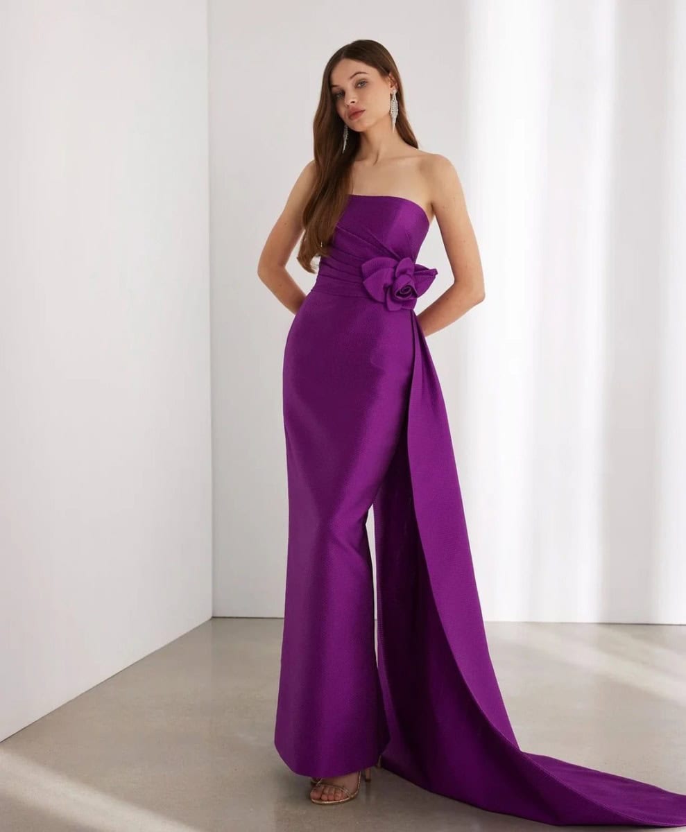Robe de soirée violette longue avec un nœud décoratif à la taille, portée par une femme dans un studio blanc.