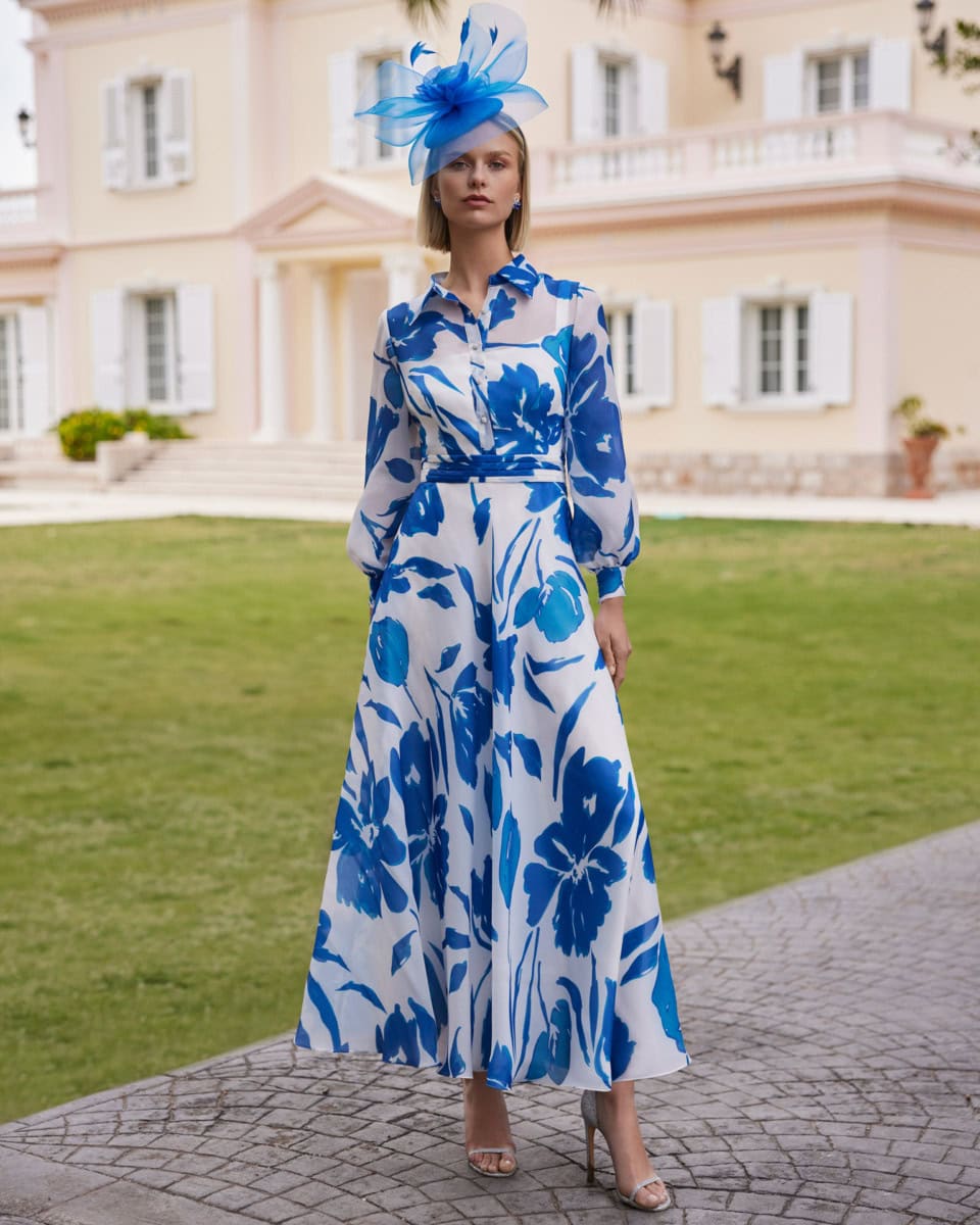 Robes élégantes de la collection O'Scarlett avec motif floral bleu et blanc, portée par une modèle devant une grande maison de style classique.
