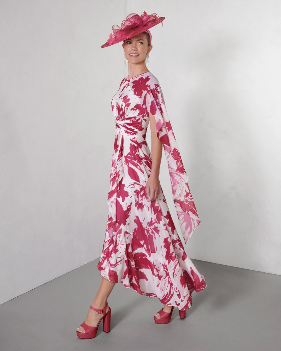 Femme élégante portant une robe longue à motif floral rose et blanc avec un chapeau assorti, style sophistiqué.