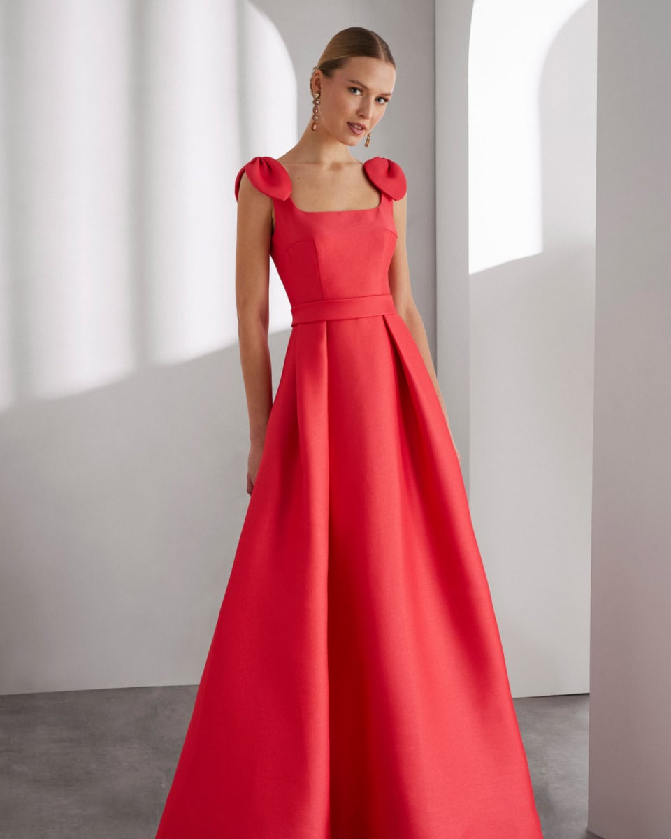 Robe de soirée rouge élégante avec épaules bouffantes et jupe longue, portée par une femme dans un décor minimaliste lumineux.