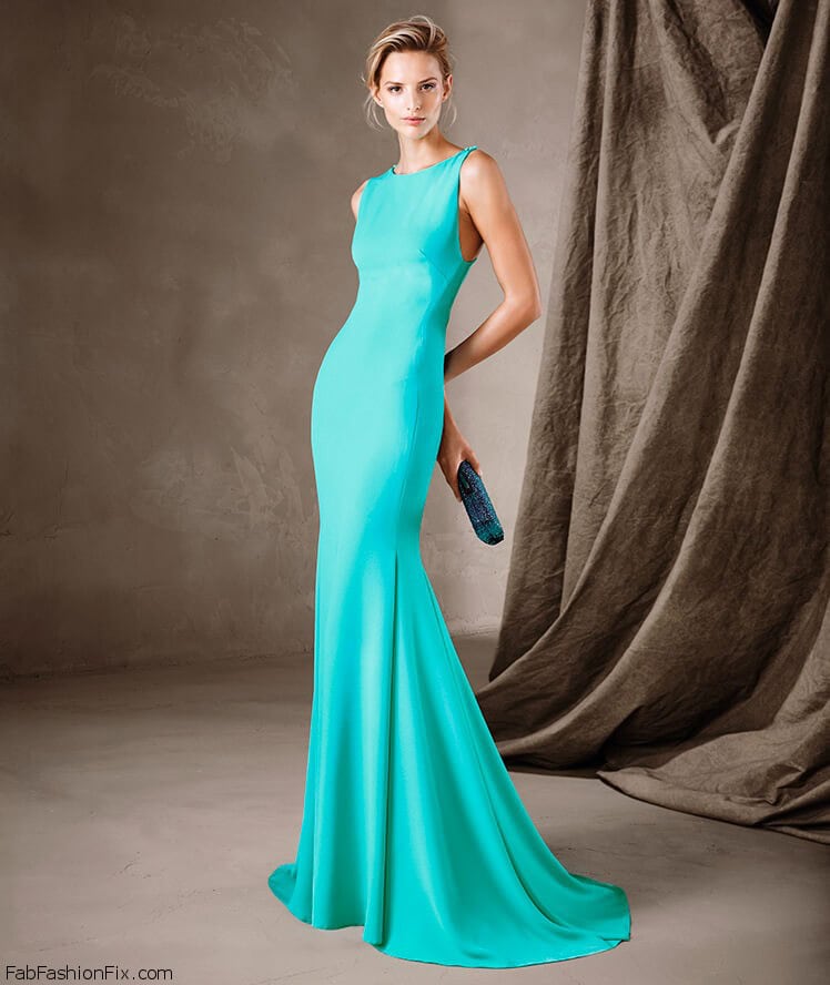 Femme portant une robe longue turquoise élégante avec un sac à main bleu, posant devant un fond neutre avec des draperies en tissu.